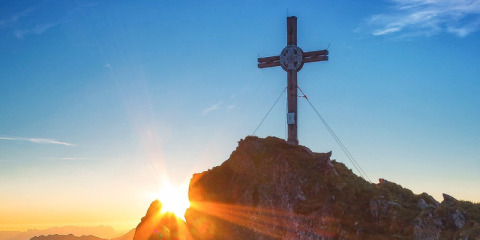 Immagine di una croce sulla cima di un monte col sole che sorge