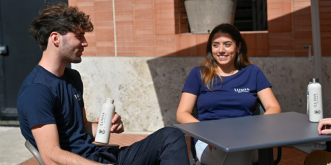 Immagine di due studenti LUMSA seduti a un tavolo con le borracce e le t-shirt del merchandising LUMSA